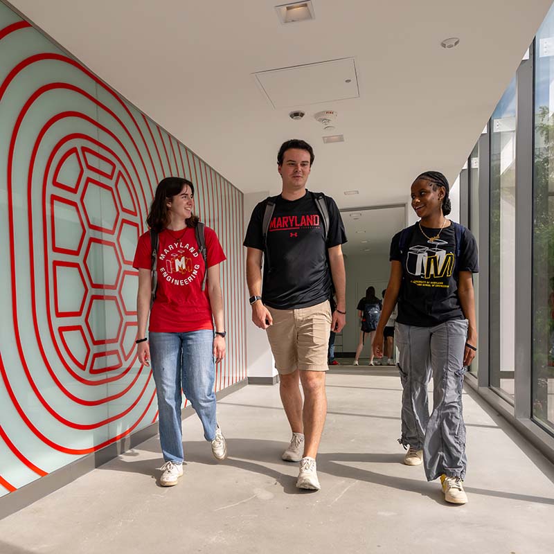 Three students walk down a hallway with a Maryland shell graphic on the wall